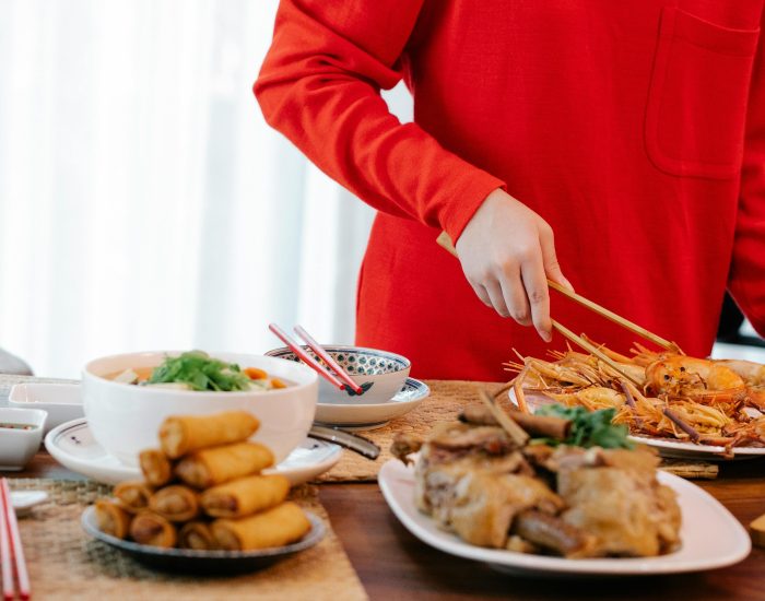 Crop unrecognizable female with tweezers serving tasty cooked prawns at table with spring rolls and stewed vegetables at home